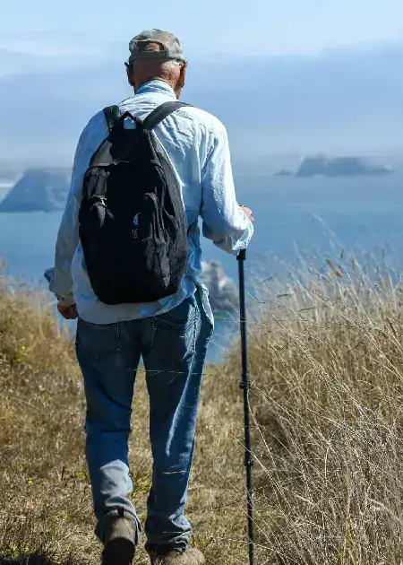 Hiker with backpack walking along coastal trail overlooking ocean view.