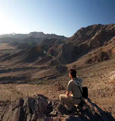 Hiker overlooking rugged mountain landscape at sunrise.