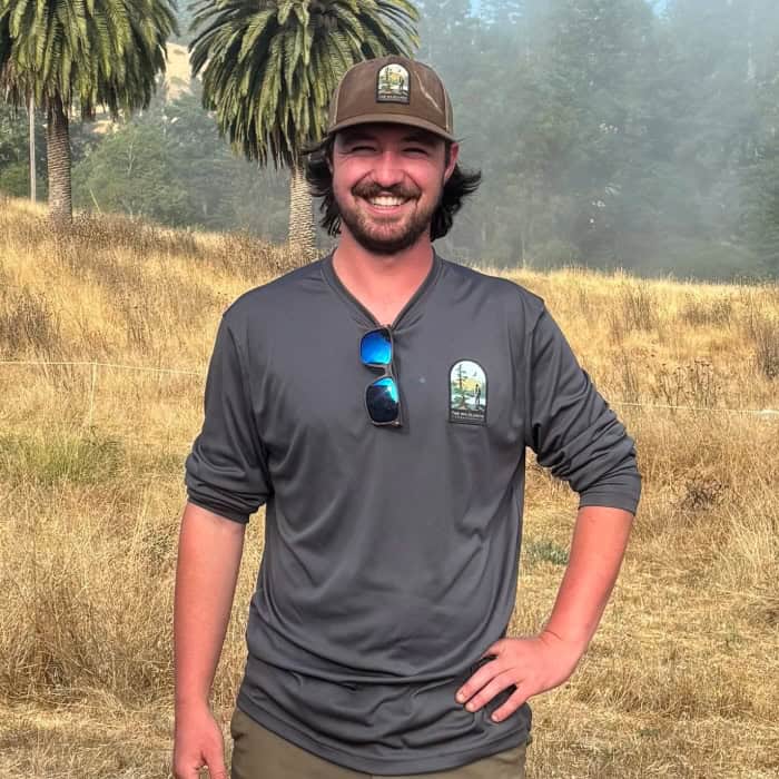 Smiling staff member in outdoor setting with trees and grass.