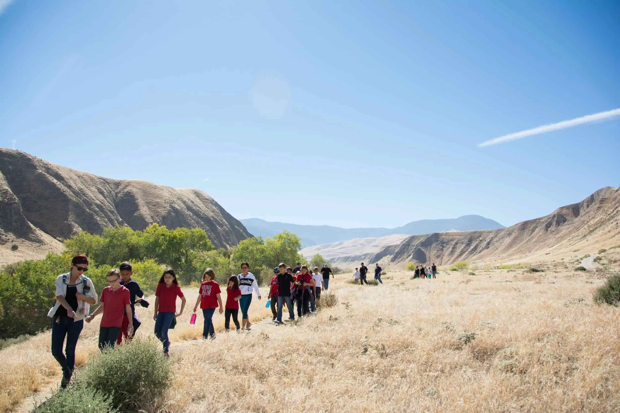 Group of people hiking through a scenic dry grassland landscape.