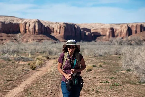 Woman hiking in desert with red rock formations in background.