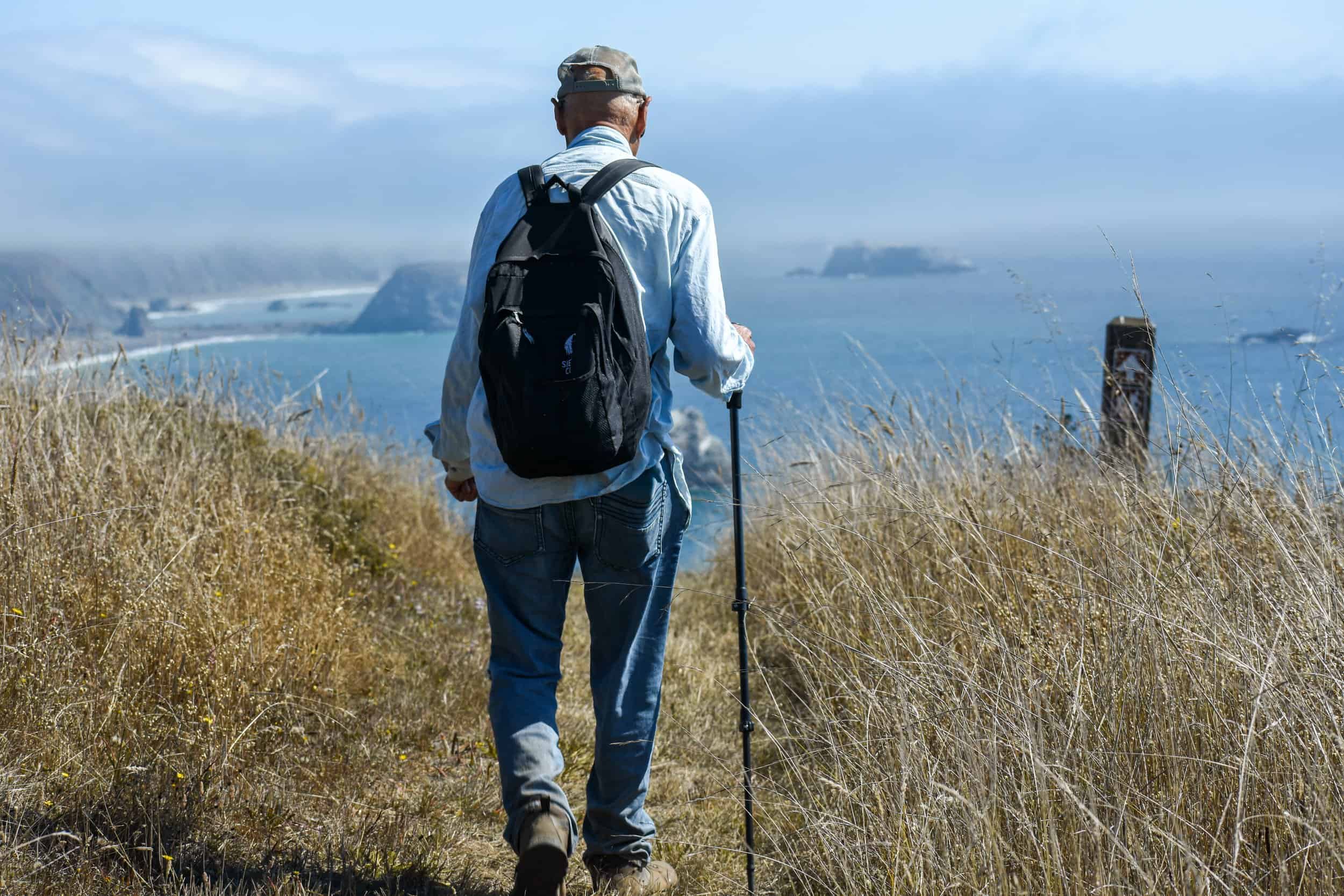 Hiker walking along coastal trail with ocean view and cliffs.