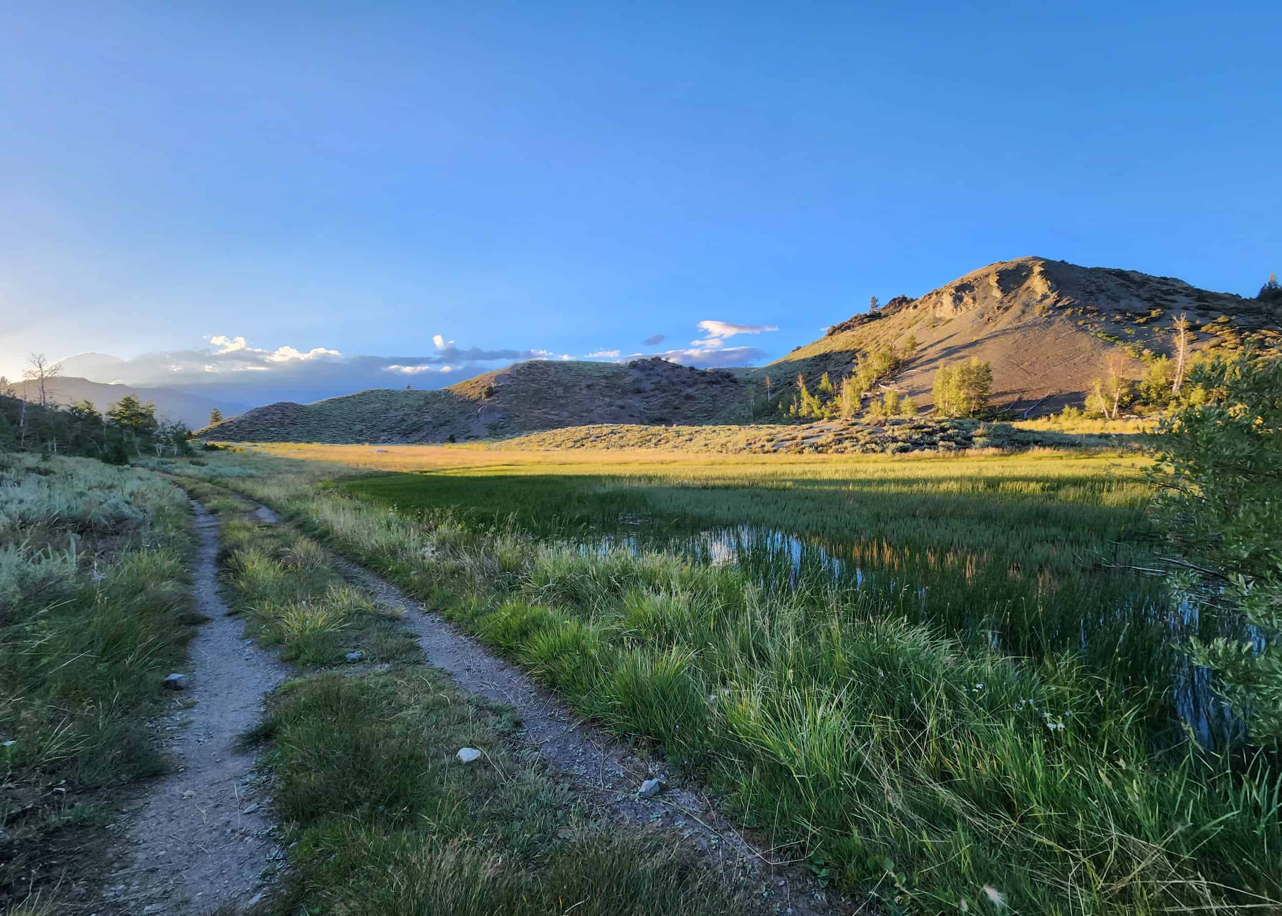 Beautiful natural landscape with mountains, fields, and a dirt trail.