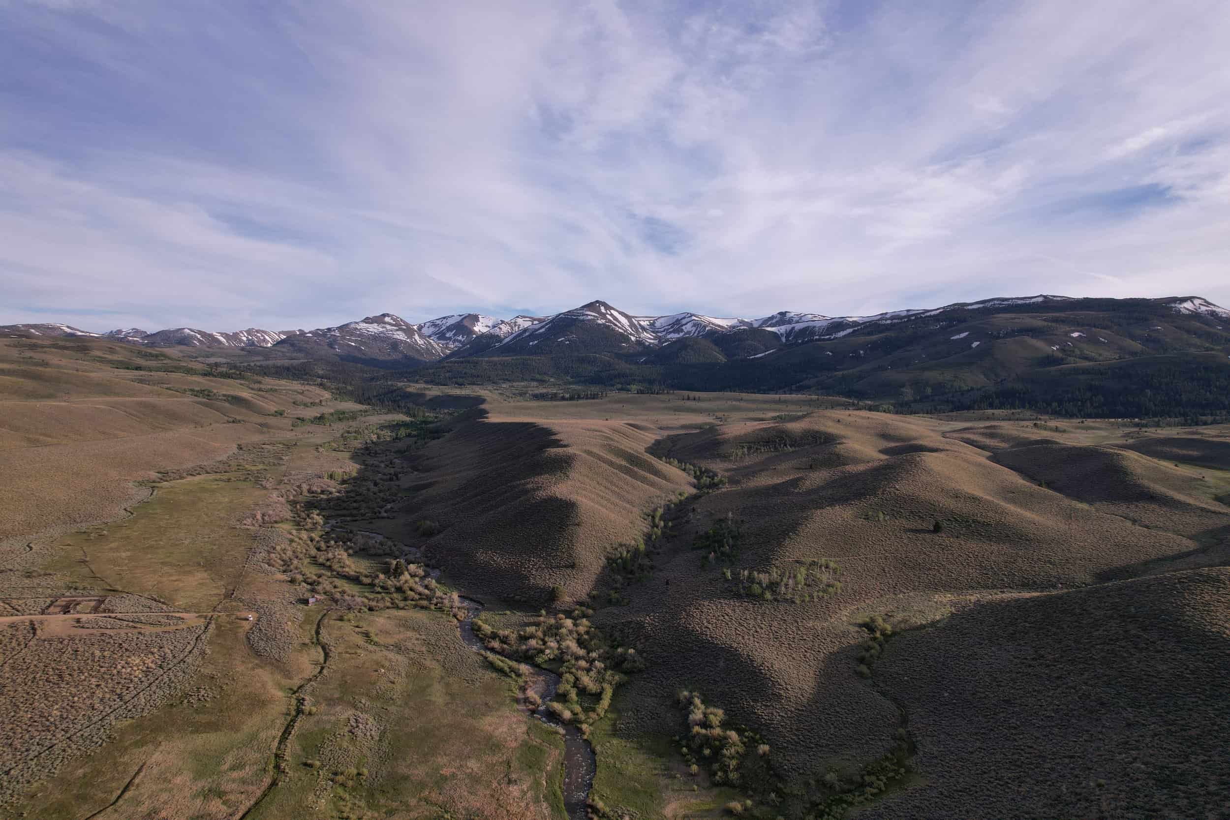 Scenic view of rolling hills and distant snow-capped mountains under a partly cloudy sky.