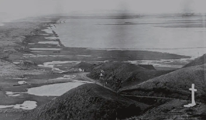 Black and white photo of a historic landscape with hills, water, and a cross.