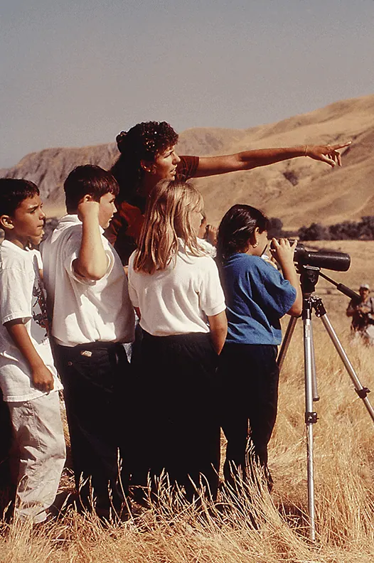 Group of children and teacher observing wildlife with telescope in nature.