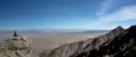 Person sitting on rocks overlooking mountain and desert view.