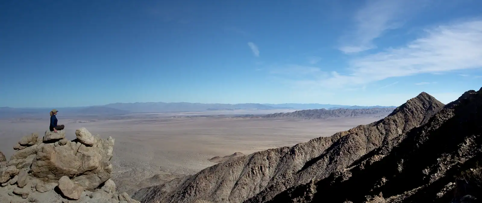 Person sitting on rocks overlooking mountain and desert view.