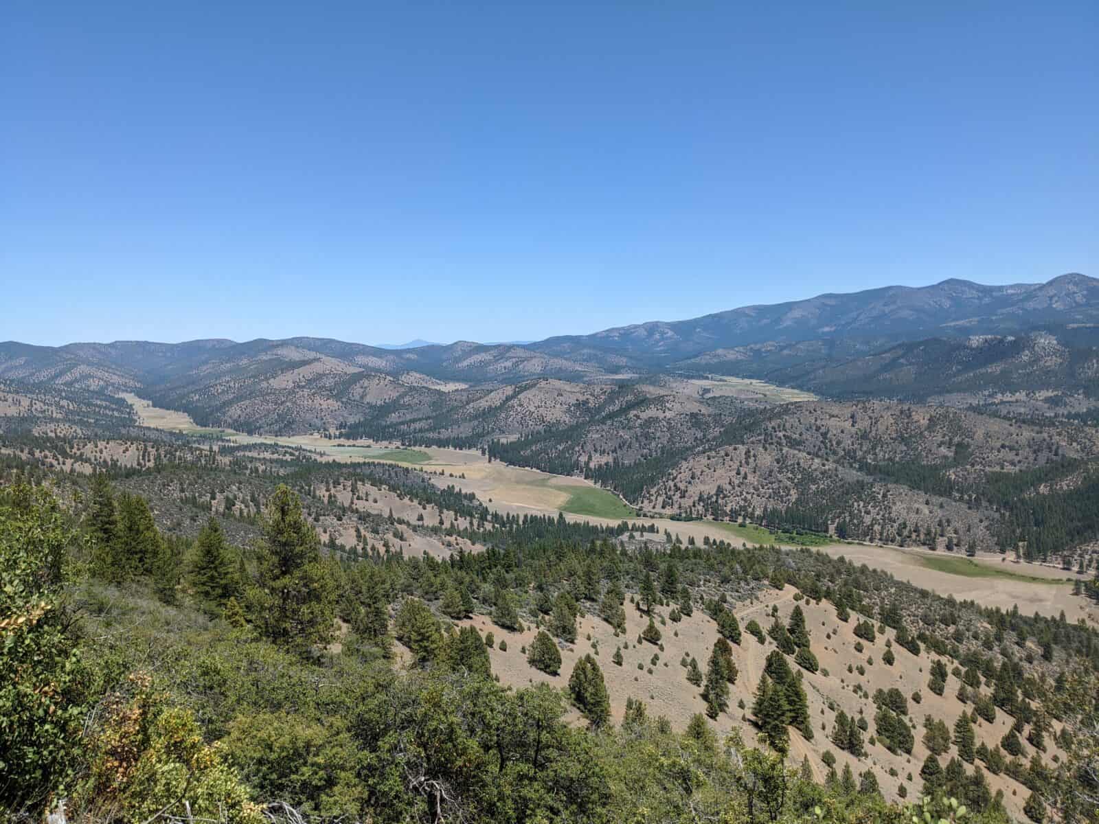 Mountain landscape with rolling hills and dense forests under a clear blue sky.