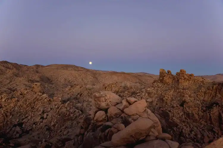 Scenic view of Pioneertown Mountains Preserve at dusk with rocky terrain and moon.