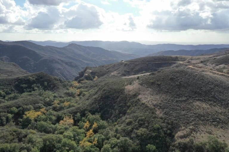 A lush green valley with rolling hills and distant mountain ranges under a partly cloudy sky.