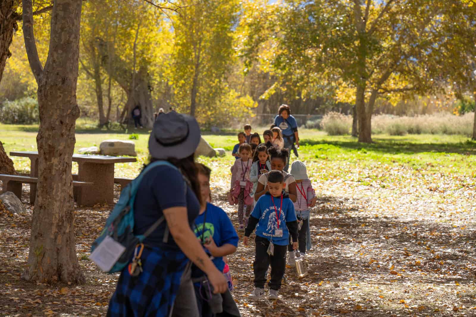 Children and adults enjoying a nature walk in a wooded park during fall.