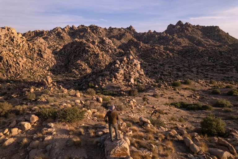 Desert mountain landscape with rocky terrain and sparse vegetation.