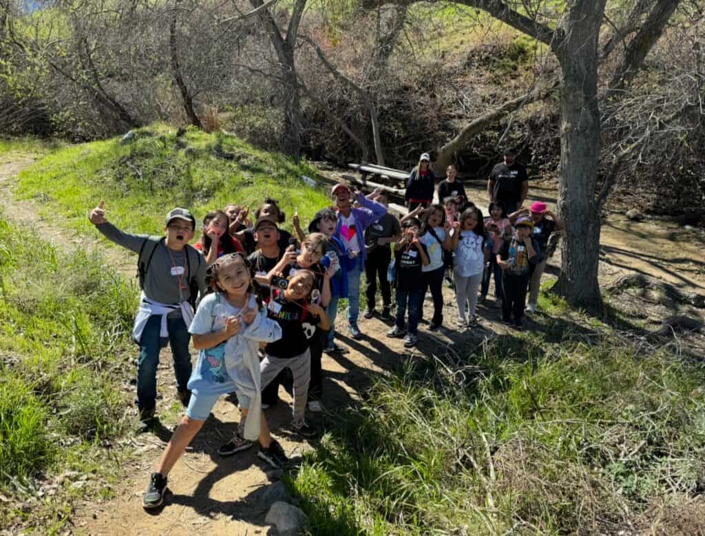 Exploring a nature trail with children and adults in a lush, wooded area during a sunny day.