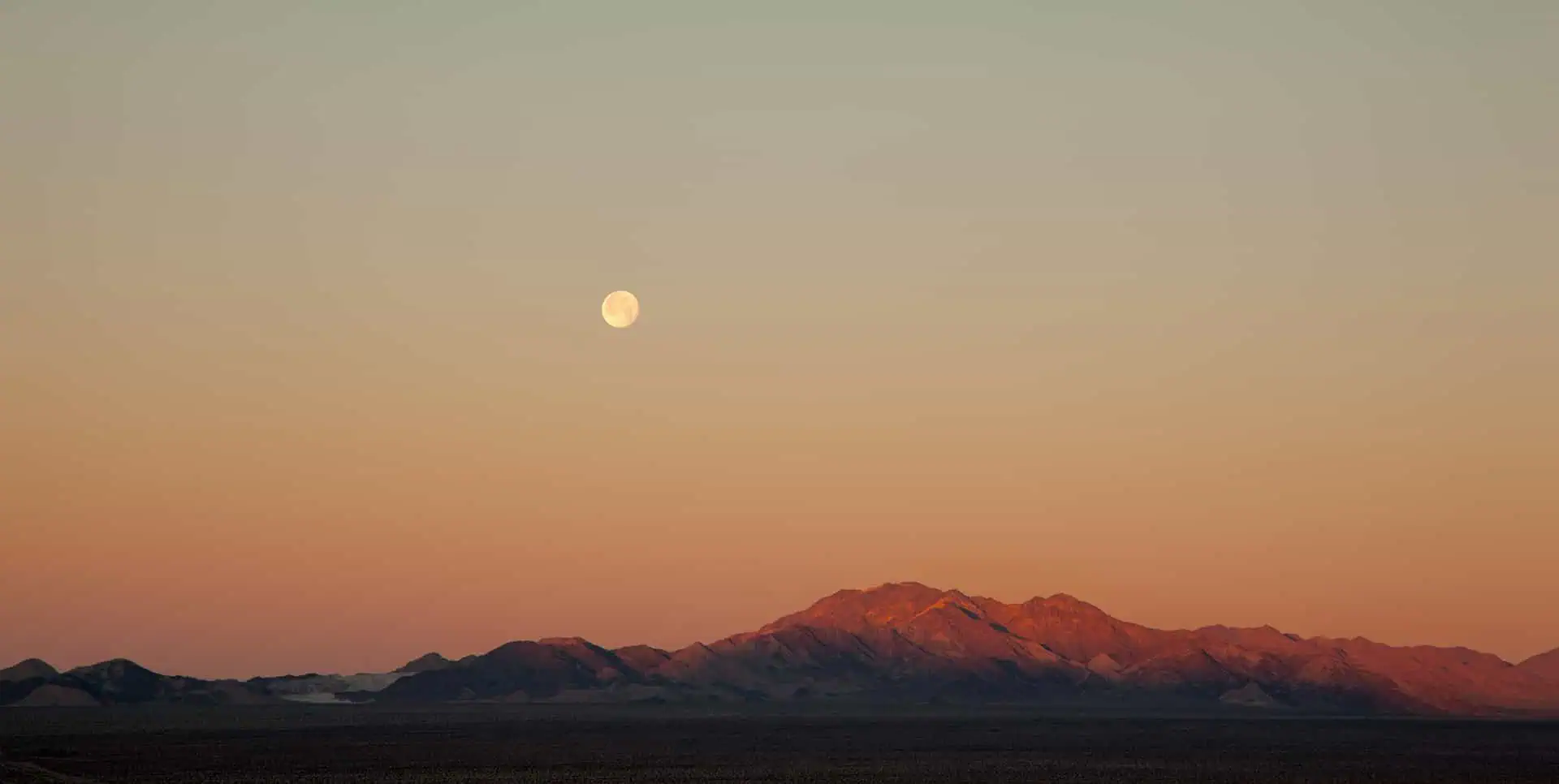 Sunset over mountain range with the moon rising in the background.