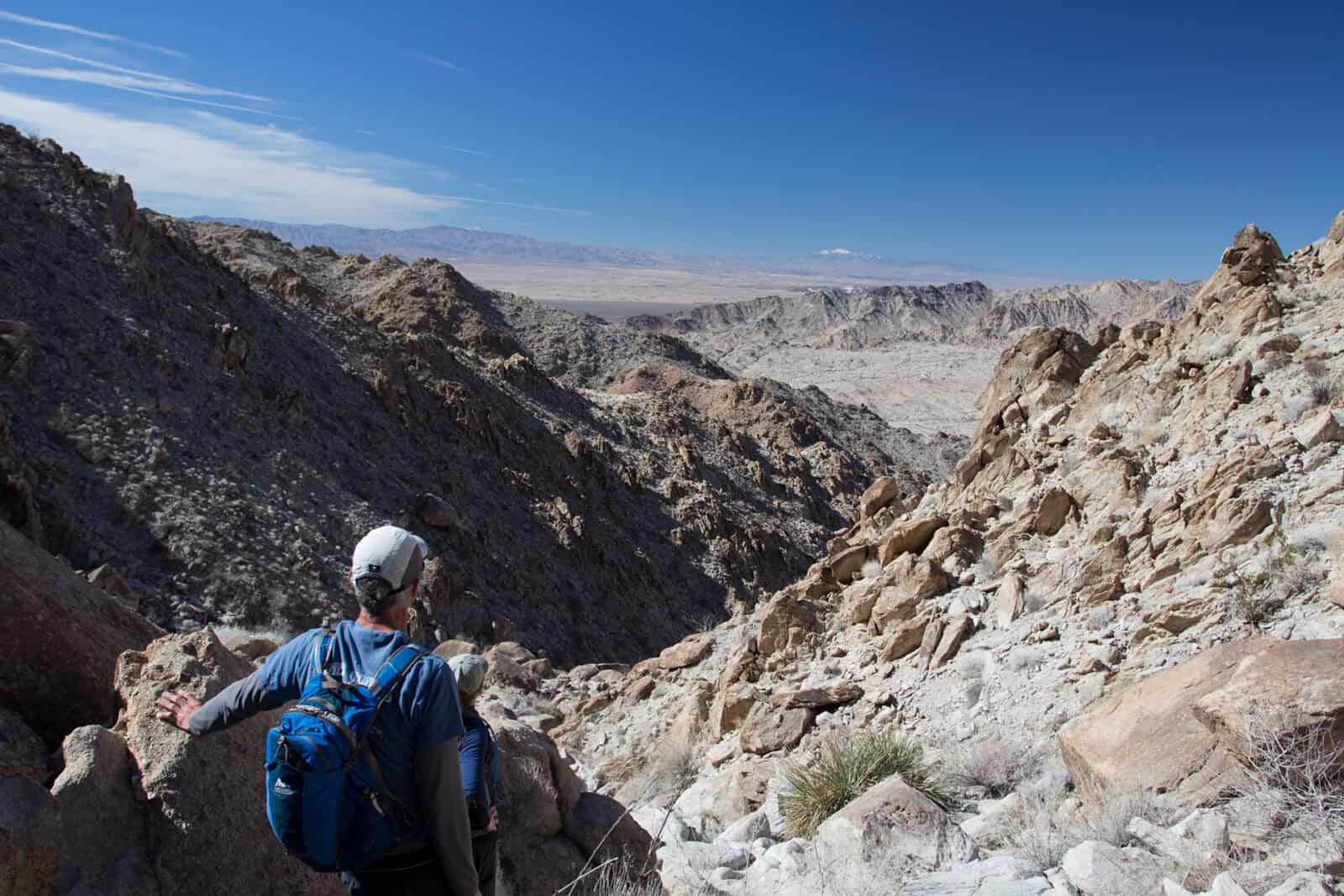 Hiker exploring a rugged desert canyon landscape with rocky terrain and clear blue sky.