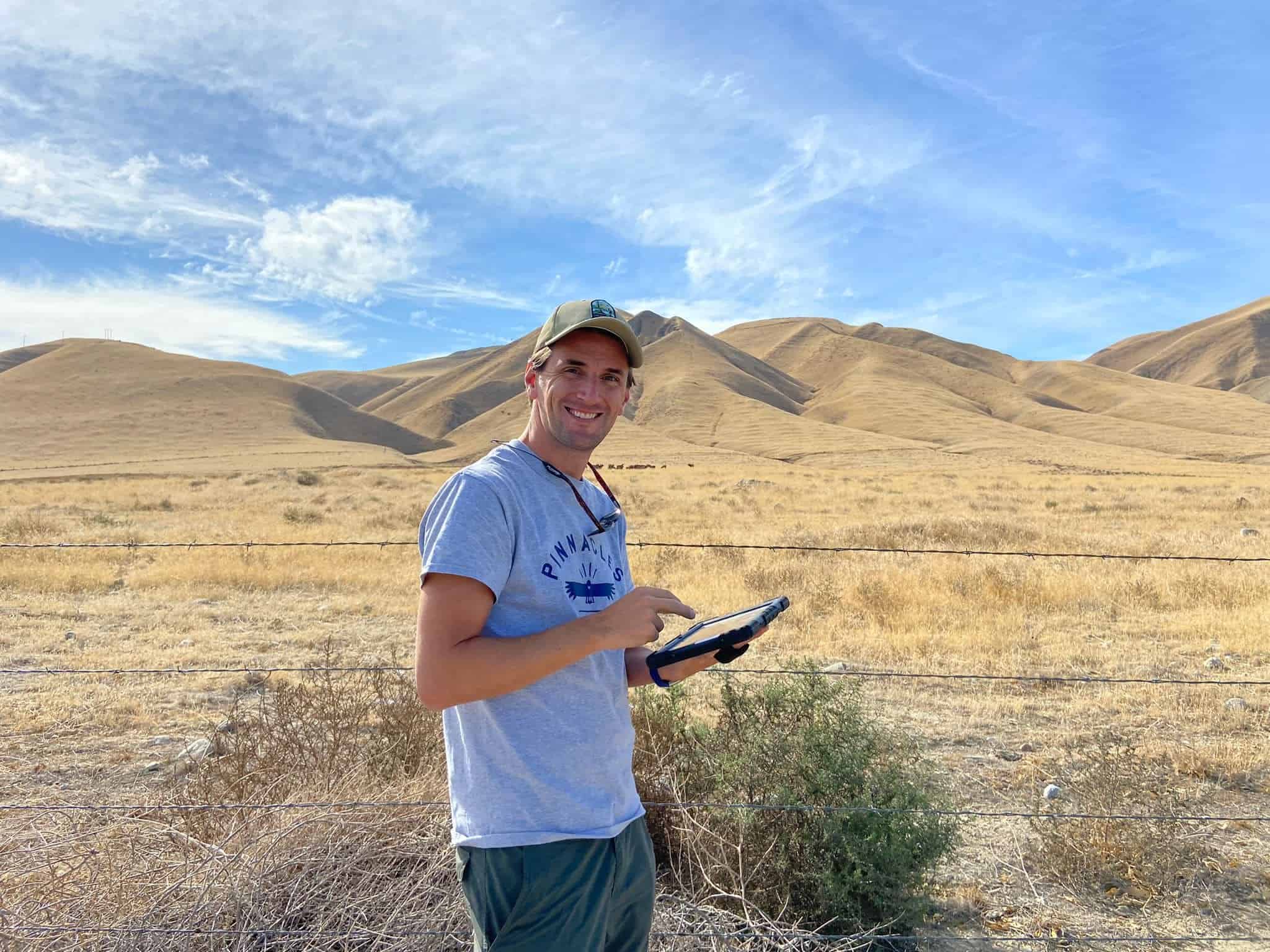 Man using a tablet in a dry, hilly landscape at The Wildlands Conservancy.