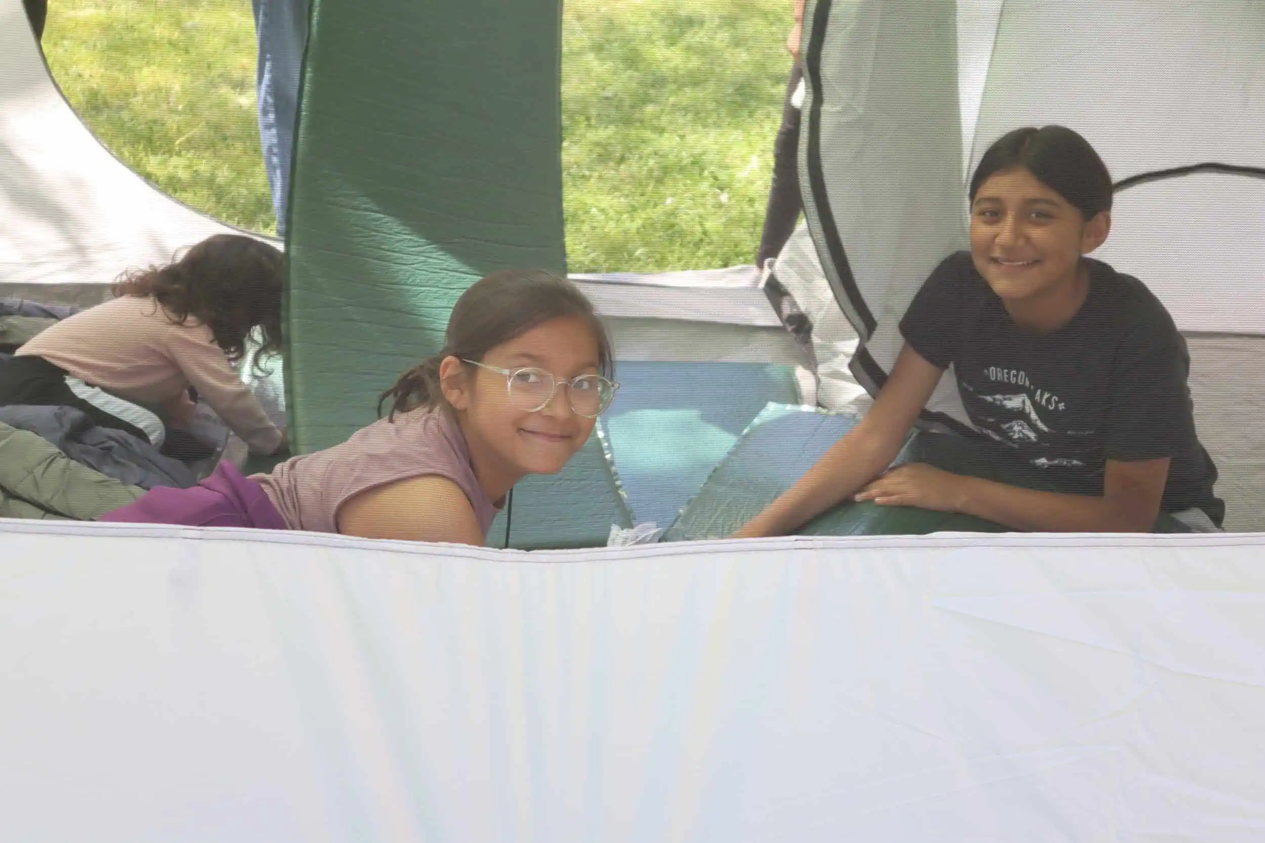 Children smiling inside a tent during outdoor nature activity.