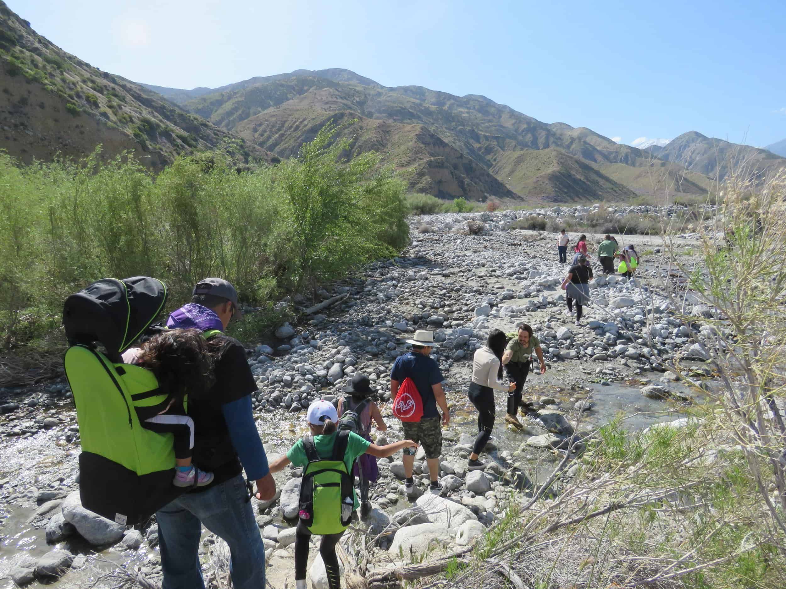Family hiking along a rocky riverbed in scenic mountain landscape.