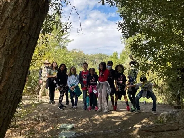 Group of children exploring a scenic outdoor preserve with trees and blue sky.