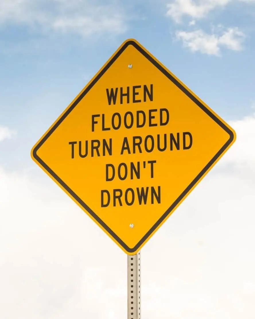 Yellow flood warning sign with black text against a blue sky background.