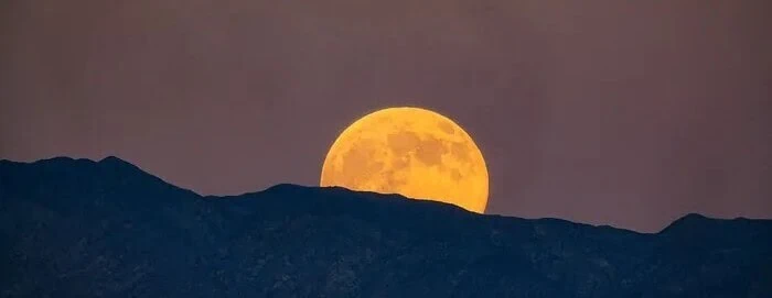 Bright full moon rising above mountain silhouette at dusk.