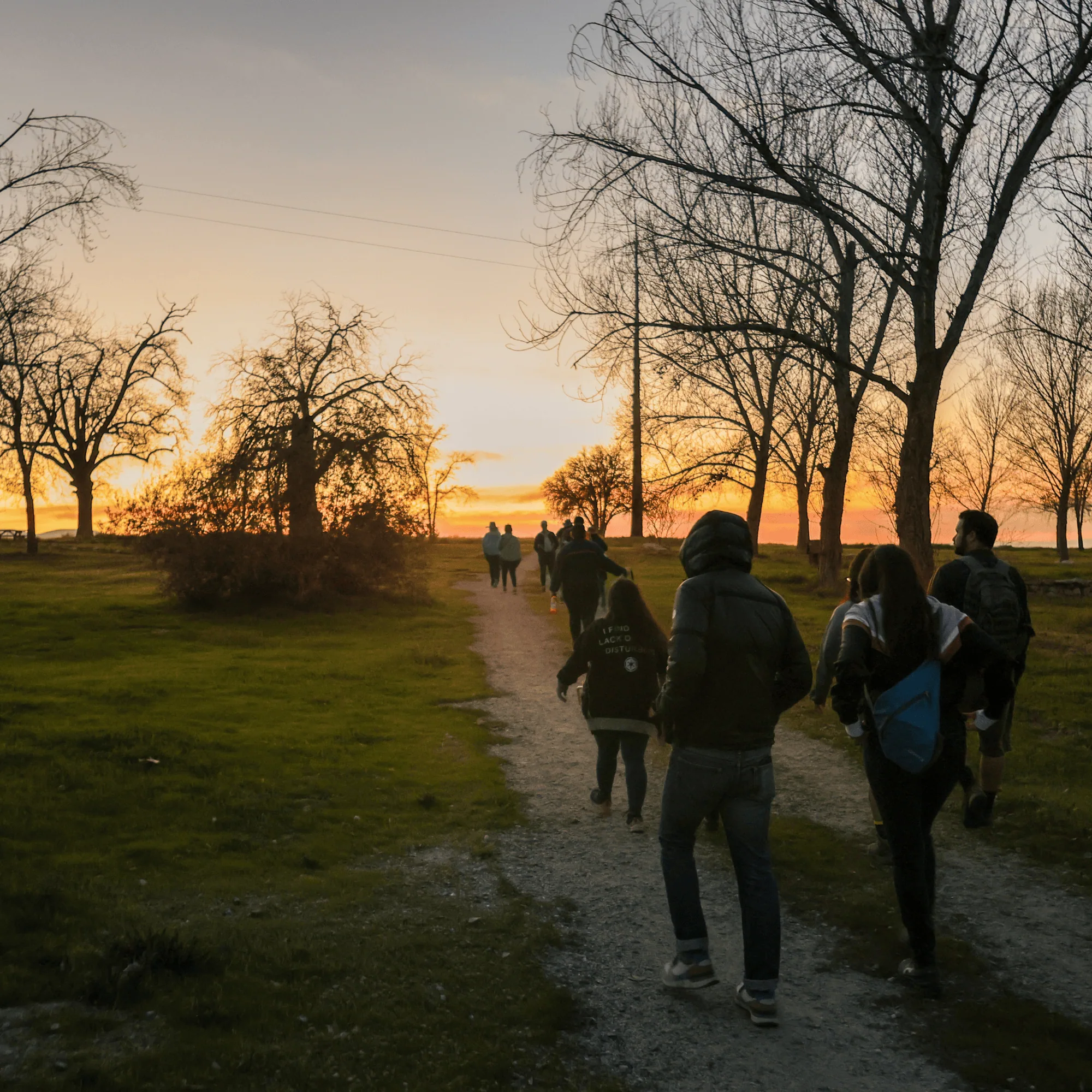 Group of people walking along a trail at sunset in a natural park setting.